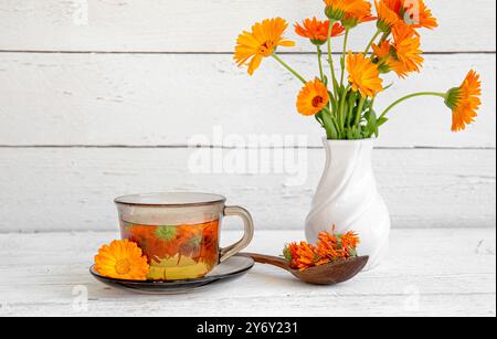 Vista laterale di Calendula officinalis la calendula, i cocci, la calendula comune o la calendula scozzese, il tè alle erbe dei fiori di pianta in vetro trasparente. Foto Stock