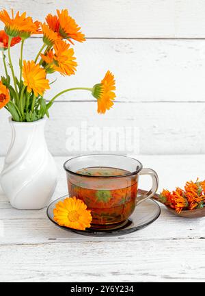 Vista laterale di Calendula officinalis la calendula, i cocci, la calendula comune o la calendula scozzese, il tè alle erbe dei fiori di pianta in vetro trasparente. Foto Stock