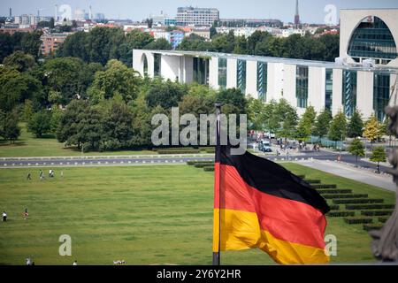 La vista panoramica cattura la Cancelleria tedesca accanto al Reichstag con la bandiera tedesca che sventolava in primo piano. Foto Stock