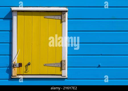 I dettagli della finestra gialla contrastano con le pareti blu della capanna sulla spiaggia di Southwold, Suffolk, Regno Unito, ad aprile Foto Stock