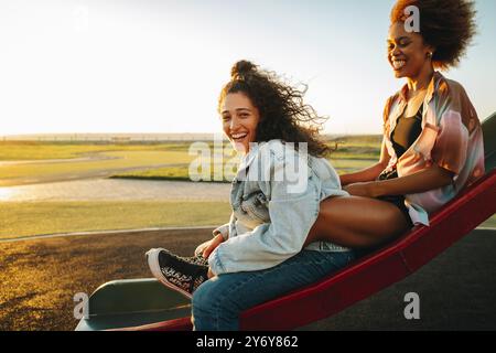 Due adolescenti che si divertono al parco, ridono gioiosamente al tramonto nel parco, condividendo un momento di felicità. Foto Stock