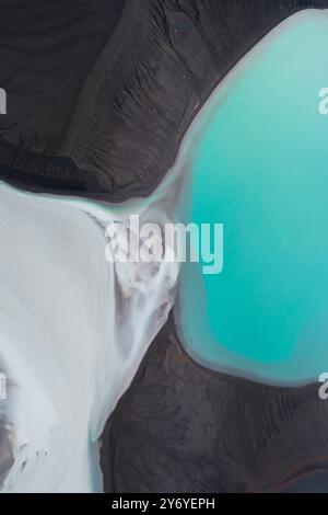 Vista aerea di un suggestivo lago turchese circondato da terreno vulcanico scuro e depositi di sedimenti bianchi. Foto Stock