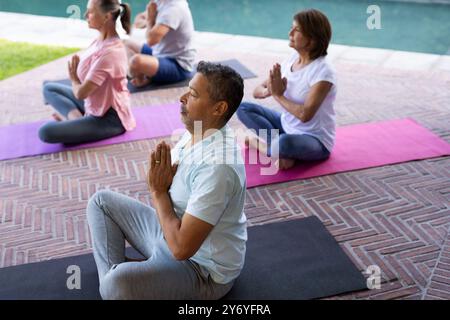 Pratica yoga a bordo piscina, amici anziani e diversi che meditano sui tappetini, a casa Foto Stock