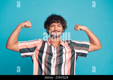 Ritratto di un giovane uomo simpatico bicipiti flessibili indossa una camicia isolata su sfondo di colore turchese Foto Stock