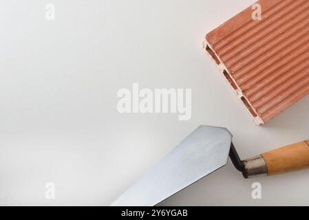 Cazzuola per muratura e costruzione con cazzuola in metallo con manico in legno e mattoni con tre fori arancioni isolati su sfondo bianco. Vista dall'alto. Foto Stock