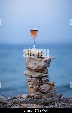 Bicchiere di vino rosa sui cairns di pietra sullo sfondo del mare sfocato Foto Stock