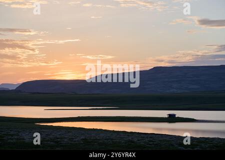 Tramonto arancione cielo nuvoloso sopra la catena montuosa e il fiume calmo Foto Stock