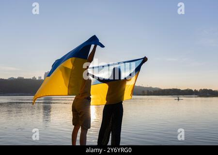 Due silhouette femminili con grande bandiera Ucraina giallo-blu dietro le spalle sullo sfondo del tramonto Foto Stock