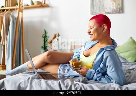 La giovane donna si rilassa comodamente sul suo letto, sorseggiando un drink e sorridendo allegramente. Foto Stock