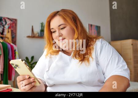 Una donna di grandi dimensioni con capelli vivaci si impegna con il suo smartphone, immersa in un'atmosfera rilassata. Foto Stock