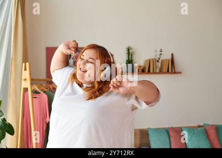 Una bella donna più grande balla felicemente a casa, immersa nella sua musica e nella sua gioia. Foto Stock