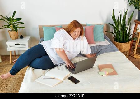 Una donna sicura di sé si impegna con il suo notebook mentre si rilassa comodamente in una camera da letto luminosa. Foto Stock