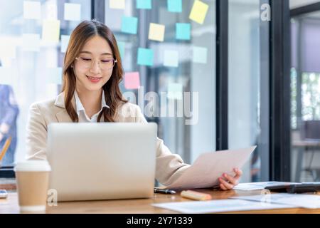 Giovane donna d'affari felice che lavora al suo progetto da sola in ufficio Foto Stock