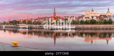 Vista panoramica del lungofiume Szczecin lungo il fiume Oder in Polonia durante l'alba, con riflessi di edifici storici e navi attraccate nelle acque calme Foto Stock