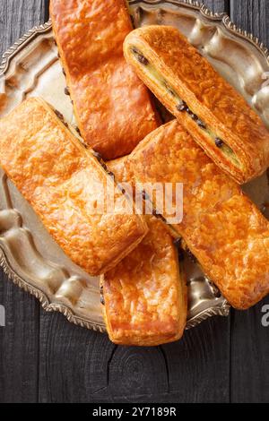 Il Pain Suisse è una deliziosa pasticceria francese fatta di pasta sfoglia ripiena di crema pasticcera e gocce di cioccolato primo piano sul piatto del tavolo. Verticale Foto Stock