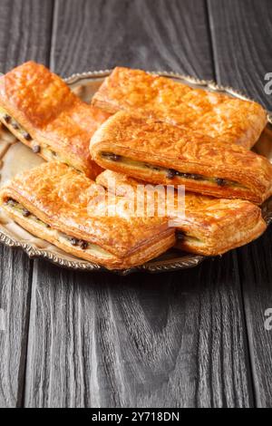 Panini francesi Pain suisse au chocolat con crema pasticcera e gocce di cioccolato da vicino in un piatto su un tavolo. Verticale Foto Stock