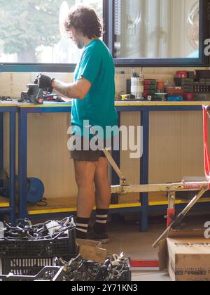 Cremona, Italia - 19 settembre 2023 meccanico con una maglietta verde stringe una parte della moto in una morsa da banco nella sua officina, usando una chiave e noi Foto Stock