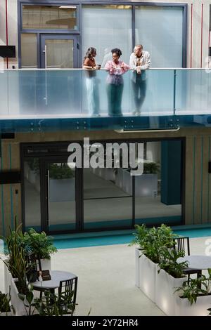 Immagine verticale di un gruppo di tre colleghi che chiacchierano mentre si trovava al secondo piano di un moderno edificio aziendale dal design minimalista, con spazio fotocopie Foto Stock