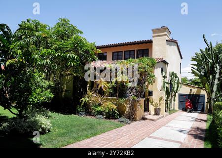 Affascinante casa in stile spagnolo con giardino lussureggiante, caratterizzata da alte palme, vegetazione e un vialetto in mattoni che conduce ad un garage. Foto Stock