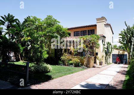 Affascinante casa in stile spagnolo con giardino lussureggiante, caratterizzata da alte palme, vegetazione e un vialetto in mattoni che conduce ad un garage. Foto Stock