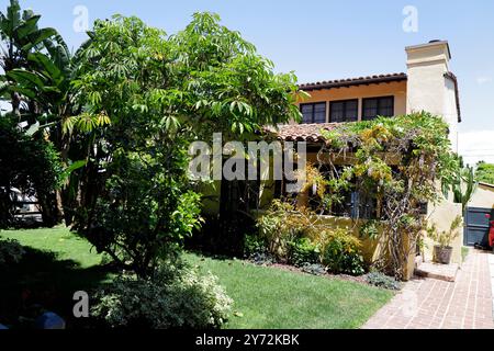 Affascinante casa in stile spagnolo con giardino lussureggiante, caratterizzata da alte palme, vegetazione e un vialetto in mattoni che conduce ad un garage. Foto Stock