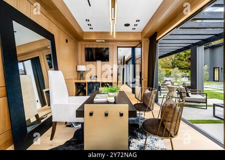 Moderno ufficio domestico con pareti in legno, grande specchio e porte in vetro che conducono ad un'area patio esterna. Foto Stock