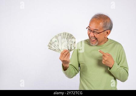 Ritratto asiatico sorridente vecchio sta tenendo un mucchio di banconote e sta puntando lo studio shot Foto Stock
