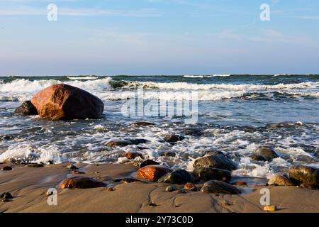 Una grande roccia poggia pacificamente sulla spiaggia di sabbia accanto al vasto oceano, creando un contrasto sorprendente con i tranquilli dintorni Foto Stock