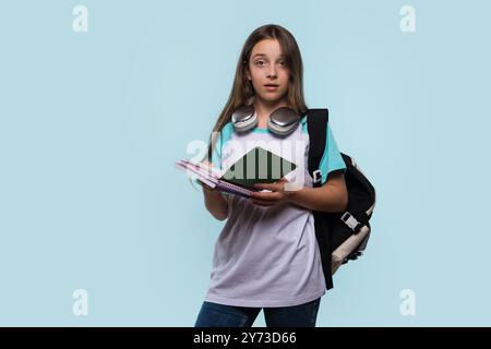 Ragazza sorpresa che tiene in mano un notebook, indossa uno zaino e le cuffie intorno al collo. Foto Stock