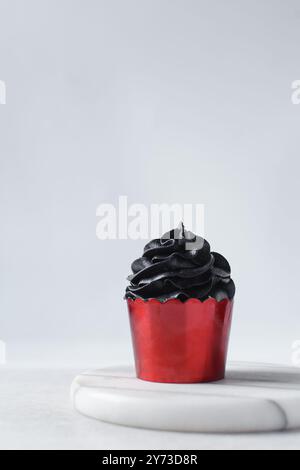 Cupcake rossi con vortice di crema di burro nero, cupcake in fodera di lamina rossa con crema di burro nero, cupcake di Halloween smerigliati su un dorso bianco Foto Stock