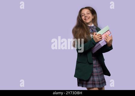 Studentessa sorridente che tiene in mano scatole regalo in uniforme. La ragazza sta saltando per la gioia Foto Stock