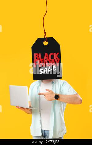 Uomo con un'etichetta invece che con la testa che regge il laptop su sfondo giallo. Promozione Black Friday Foto Stock