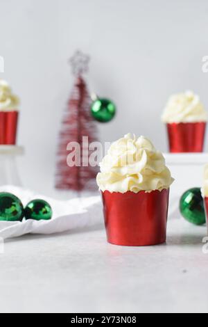 Cupcake natalizi rossi con vortice di crema di burro, cupcake in fodera di lamina rossa con crema alla vaniglia, cupcake smerigliati e ornamenti natalizi Foto Stock