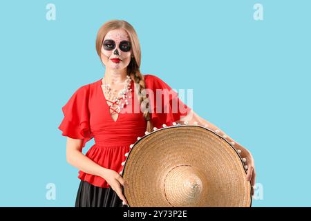 Giovane donna con cappello sombrero dipinto teschio sul viso su sfondo blu. Celebrazione del giorno dei morti in Messico (El dia de Muertos) Foto Stock