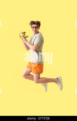 Giovane con occhiali da sole con banane che saltano su sfondo giallo Foto Stock