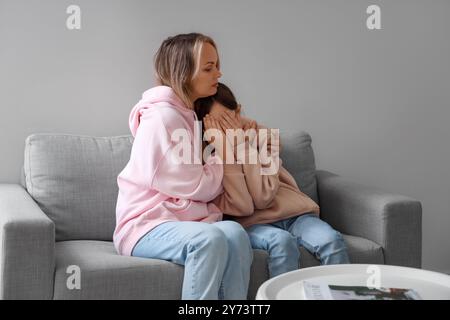 Madre che abbraccia sua figlia piangente sul divano a casa. Concetto di difficoltà familiari Foto Stock