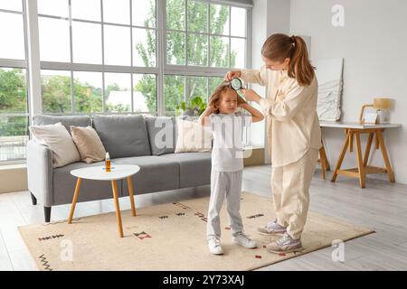 Madre con lente d'ingrandimento che controlla i capelli della sua bambina con pediculosi a casa Foto Stock