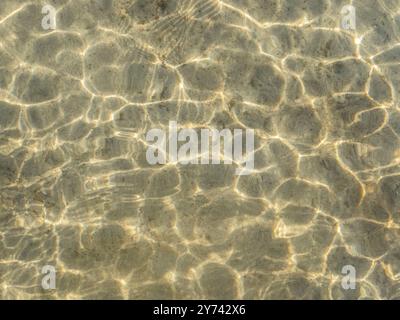 La consistenza della sabbia e i riflessi della luce sull'acqua leggermente increspata. Superficie dell'acqua di ondulazione. Foto Stock