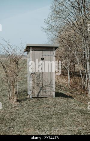 Un WC esterno in legno in stile retrò con un cuore tagliato sulla porta in primavera Foto Stock