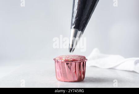 Creare una crema di burro nera su un cupcake rosa, decorare i cupcake, applicare una glassa alta sui cupcake, il processo di decorazione del cupcake Foto Stock