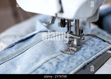 Primo piano del piede di una macchina da cucire per creare un punto sui jeans blu. Foto Stock