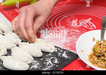 Una donna scolpisce gnocchi di impasto con il ripieno di carne in cucina. Cucinare deliziosi gnocchi fatti in casa Foto Stock