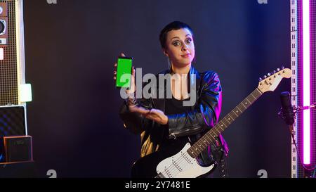 Musicista rock donna che suona la chitarra accanto a un display con schermo verde sul dispositivo, mentre esegue un'esibizione di musica dal vivo sul palco del nightclub. Il rocker dell'artista si comporta alla moda e ribelle con uno stile audace. Telecamera A.. Foto Stock