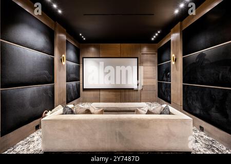 Una moderna sala home Theater con comode poltrone, un grande schermo, eleganti pannelli in legno e pareti acustiche nere. Foto Stock
