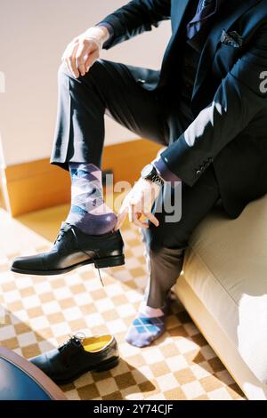 L'uomo in tuta indossa scarpe in pelle nera mentre è seduto sul letto Foto Stock
