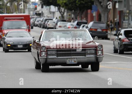 Una classica cabriolet rossa Cadillac rotola lungo una strada della città con i passeggeri che lampeggiano segnali di pace, incarnando un'atmosfera rilassata e vintage. Foto Stock