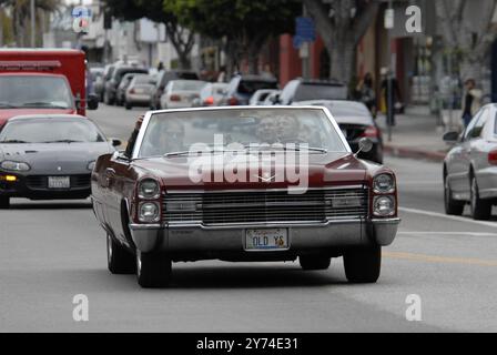 Una classica cabriolet rossa Cadillac rotola lungo una strada della città con i passeggeri che lampeggiano segnali di pace, incarnando un'atmosfera rilassata e vintage. Foto Stock