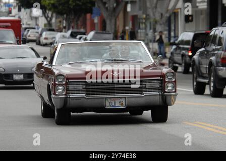 Una classica cabriolet rossa Cadillac rotola lungo una strada della città con i passeggeri che lampeggiano segnali di pace, incarnando un'atmosfera rilassata e vintage. Foto Stock