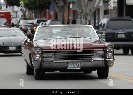 Una classica cabriolet rossa Cadillac rotola lungo una strada della città con i passeggeri che lampeggiano segnali di pace, incarnando un'atmosfera rilassata e vintage. Foto Stock