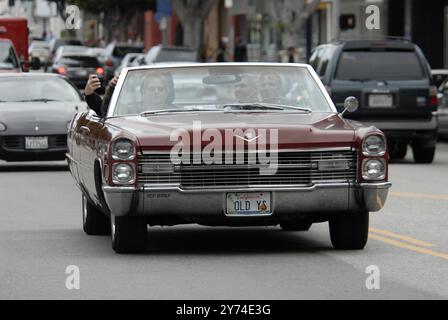 Una classica cabriolet rossa Cadillac rotola lungo una strada della città con i passeggeri che lampeggiano segnali di pace, incarnando un'atmosfera rilassata e vintage. Foto Stock